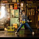 Marty stands holding his guitar legs apart and hand raised - a classic rock 'n' roll pose. Beside him the speaker has blown up producing sparks