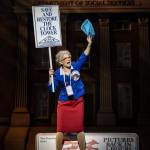 A woman stands on a bench holding a leaflet and a placard that reads: Save The Hill Valley Clock Tower