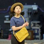 Victoria Chen wearing a hat and yellow bag with her hands in front of her and looking over.