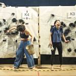 Ami Okumura Jones holding a wooden bucket and Victoria Chen standing in front of a wall and reacting to the soot sprites.